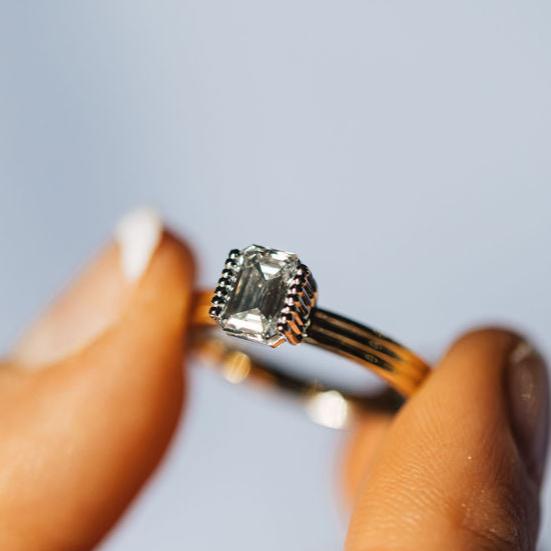 Model holding ring with a emerald cut diamond on a yellow gold band.