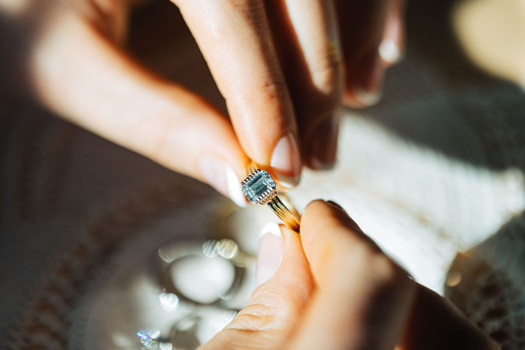 Model holding ring with a emerald cut diamond on a yellow gold band.